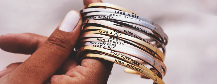 Een hand die een stapel gouden en zilveren armbanden vasthoudt met verschillende ingegraveerde zinnen.