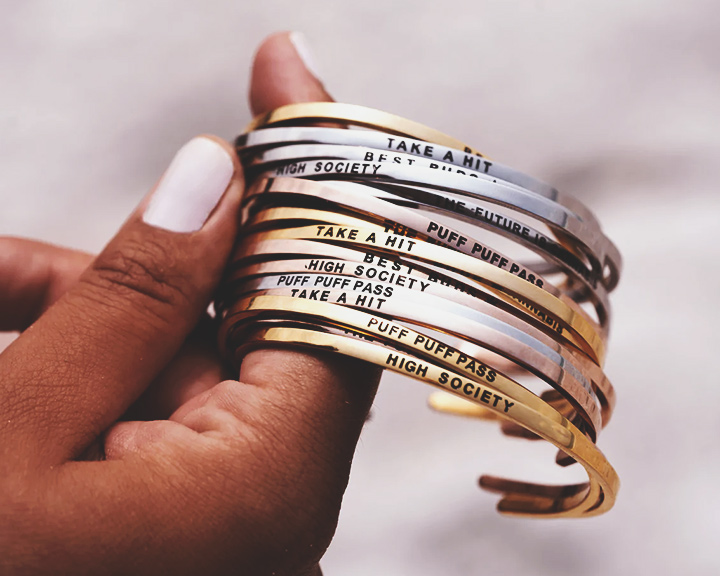 Een hand die een stapel gouden en zilveren armbanden vasthoudt met verschillende ingegraveerde zinnen.