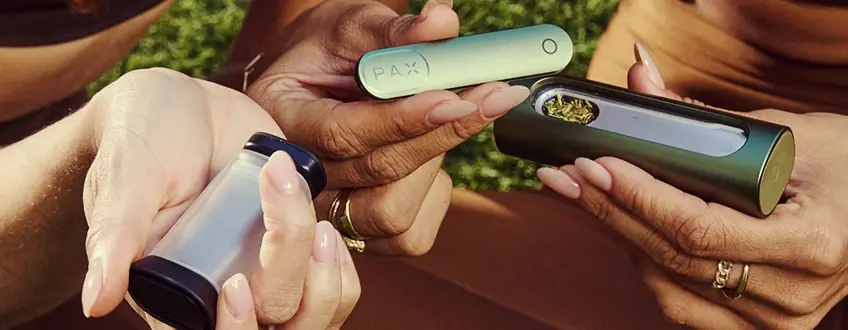 Vullen van de Pax Flow Vaporizer Twee handen die samen de Pax Flow vaporizer vullen met gemalen cannabis uit een kleine grinder, ter illustratie van het eenvoudige vulproces buiten op groen gras.