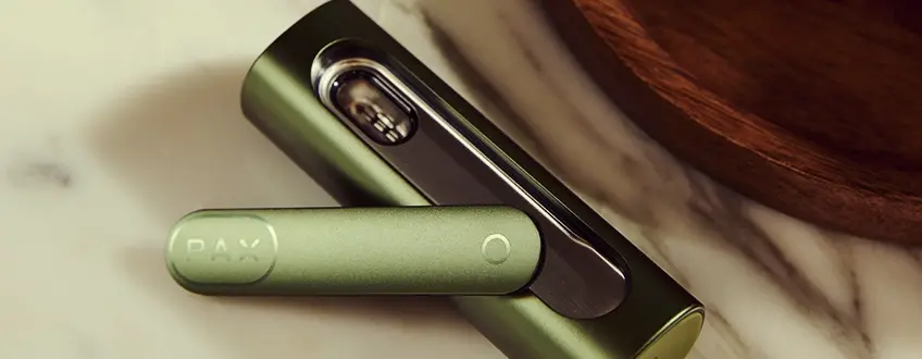 Geopende Pax Flow Vaporizer Close-up van de geopende Pax Flow vaporizer die de interne kamer vol cannabis onthult, vastgehouden door een hand in een casual buitenomgeving met natuurlijk licht.
