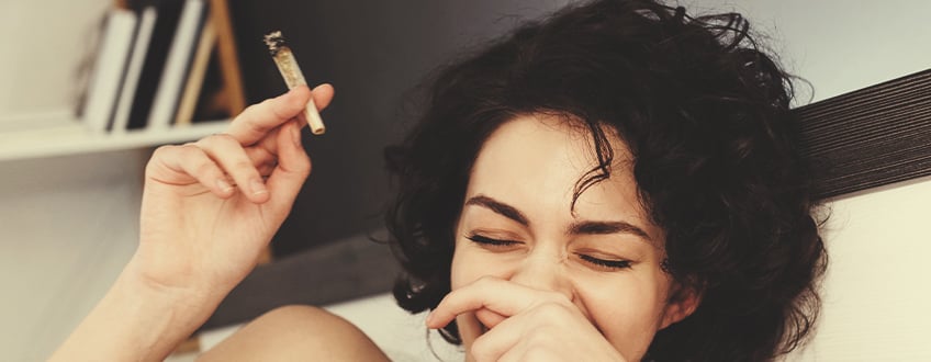 Persoon die lacht terwijl hij een cannabisjoint vasthoudt.