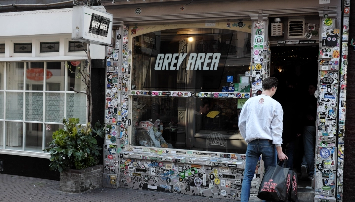 Ingang van een cannabiscoffeeshop in Nederland met een Grey Area-bord en een met stickers bedekte gevel.