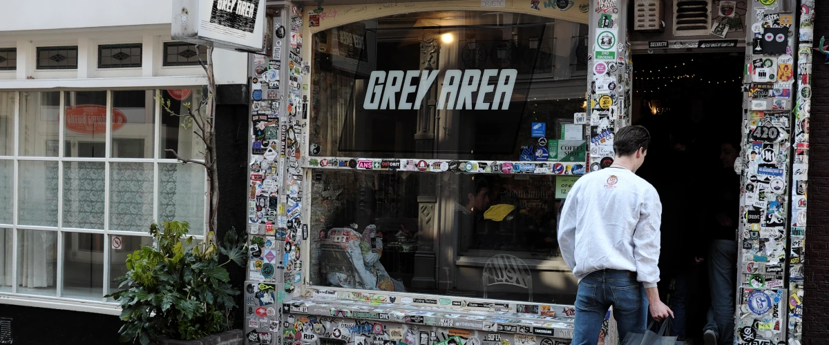 Ingang van een cannabiscoffeeshop in Nederland met een Grey Area-bord en een met stickers bedekte gevel.