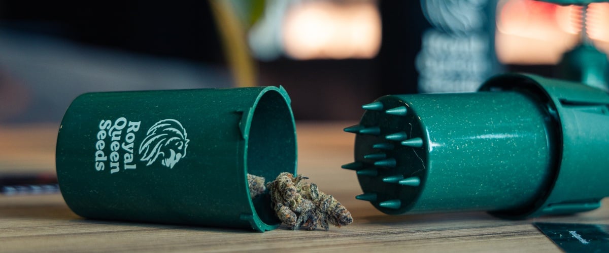 Afbeelding van een compacte grindtainer met cannabis toppen op een houten oppervlak.