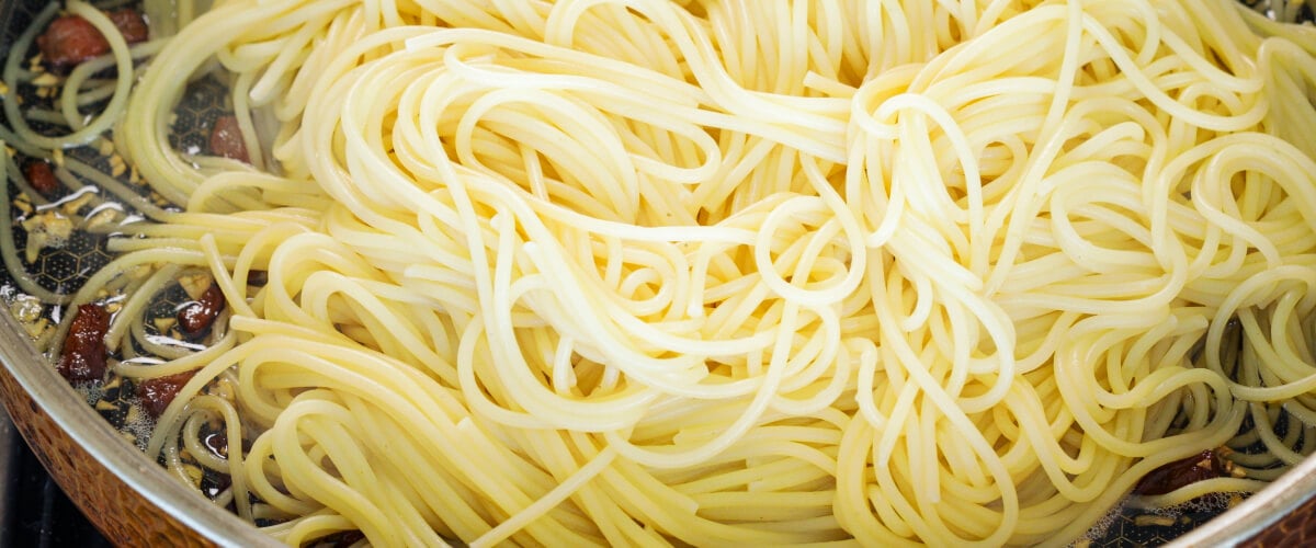 Uitgelekte spaghetti mengen met knapperige pancetta en geïnfuseerde boter in een pan, vierde stap voor cannabis-geïnfuseerde carbonara