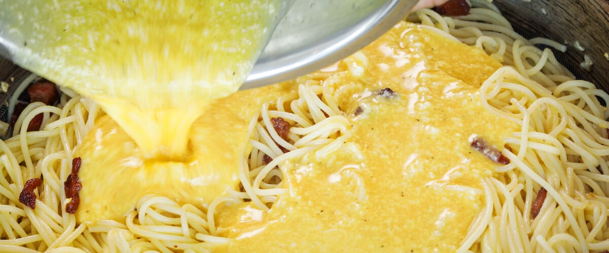 Eier- en kaasmengsel gieten over hete spaghetti in een pan, vijfde stap voor cannabis-geïnfuseerde carbonara